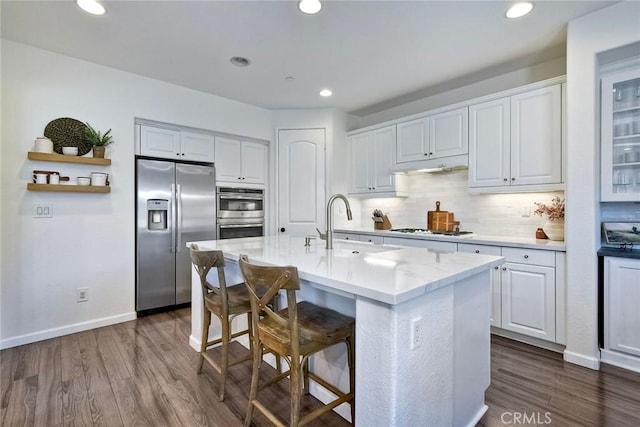 kitchen with a breakfast bar area, appliances with stainless steel finishes, a kitchen island with sink, white cabinetry, and dark hardwood / wood-style flooring