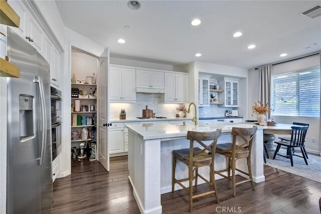 kitchen with dark wood-type flooring, white cabinetry, a kitchen breakfast bar, a center island with sink, and stainless steel fridge with ice dispenser