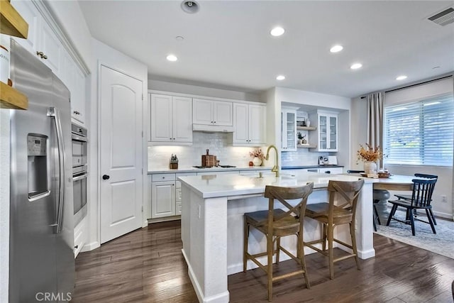 kitchen with white cabinetry, stainless steel appliances, a center island with sink, dark hardwood / wood-style flooring, and decorative backsplash