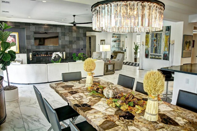 dining area with tile walls, ceiling fan with notable chandelier, and a tile fireplace