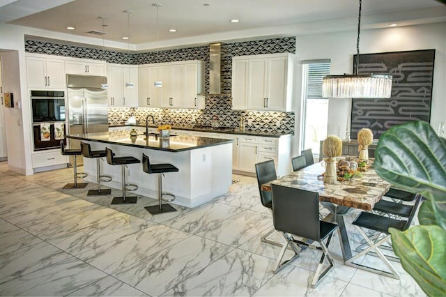 kitchen featuring white cabinetry, wall chimney range hood, stainless steel fridge with ice dispenser, and an island with sink