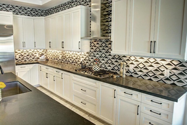 kitchen featuring wall chimney range hood, dark stone countertops, sink, appliances with stainless steel finishes, and white cabinets