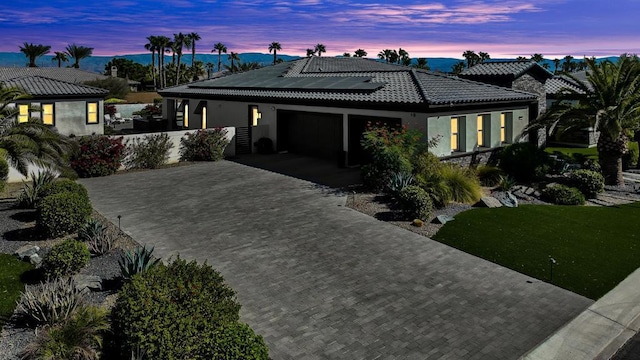 back house at dusk featuring a lawn, solar panels, and a garage