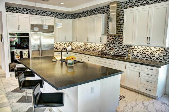 kitchen with stainless steel appliances, a center island with sink, and wall chimney range hood