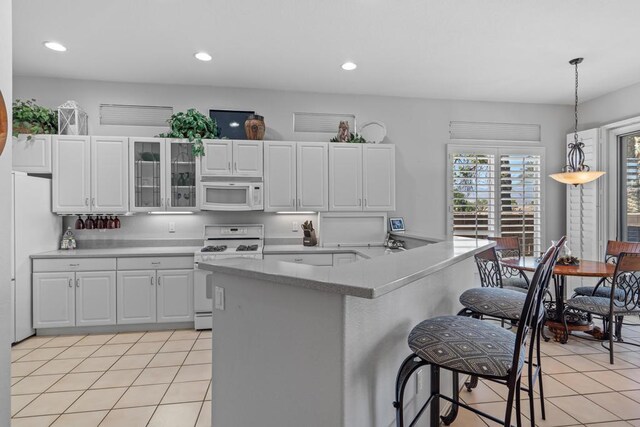 kitchen featuring a kitchen bar, white appliances, light tile patterned floors, white cabinets, and hanging light fixtures