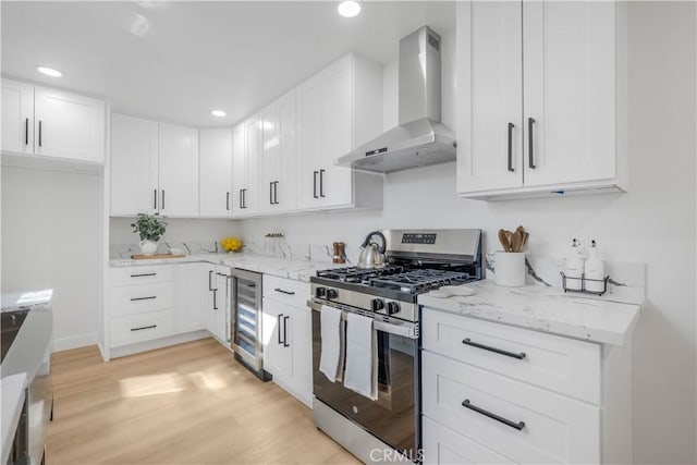 kitchen with light wood-type flooring, wall chimney exhaust hood, white cabinetry, wine cooler, and stainless steel range with gas stovetop