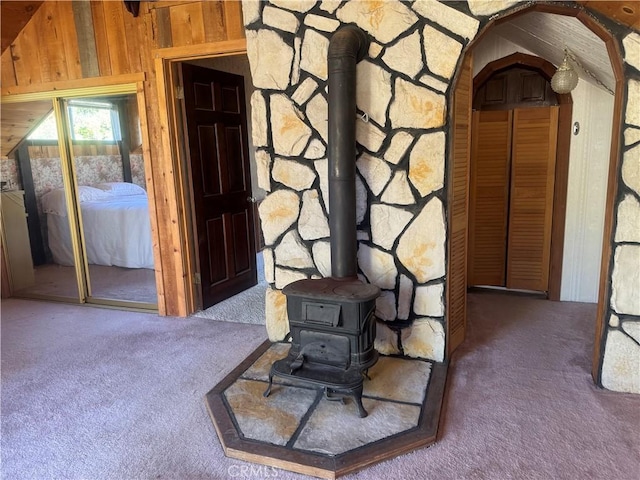 interior space featuring a wood stove, wooden walls, and dark colored carpet