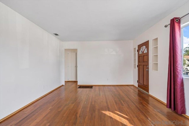 spare room featuring built in shelves and dark hardwood / wood-style flooring