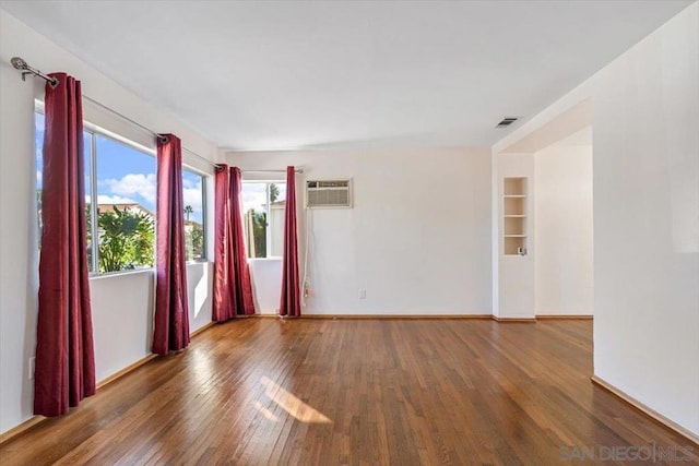 empty room featuring built in shelves, dark hardwood / wood-style flooring, and an AC wall unit