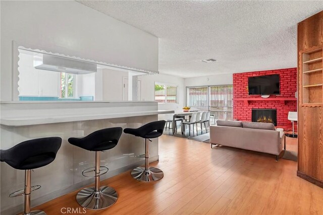 kitchen with a kitchen breakfast bar, a brick fireplace, a textured ceiling, and light wood-type flooring