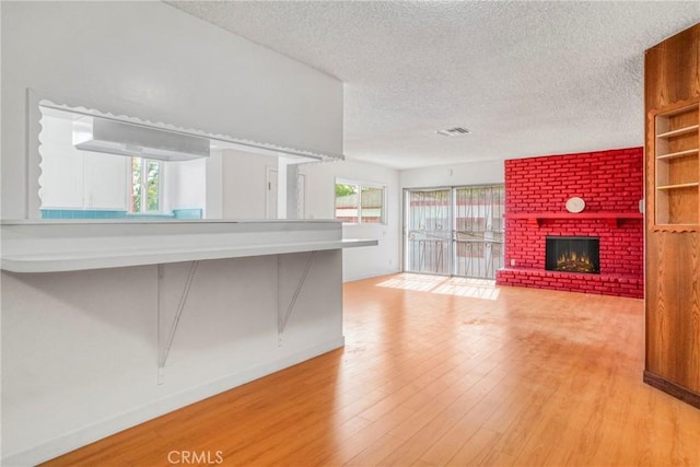 unfurnished living room with light hardwood / wood-style floors, a textured ceiling, and a brick fireplace