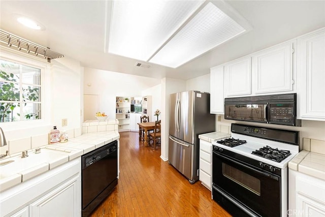 kitchen with white cabinetry, tile counters, black appliances, and light hardwood / wood-style floors