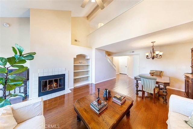 living room with ceiling fan with notable chandelier, beam ceiling, hardwood / wood-style flooring, high vaulted ceiling, and a tiled fireplace