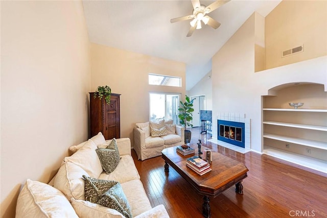 living room with high vaulted ceiling, ceiling fan, dark wood-type flooring, and a tiled fireplace