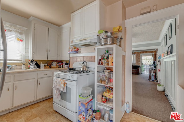 kitchen with white gas stove, a textured ceiling, light carpet, white cabinets, and exhaust hood