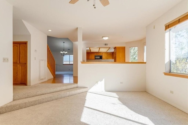 carpeted empty room featuring ceiling fan with notable chandelier