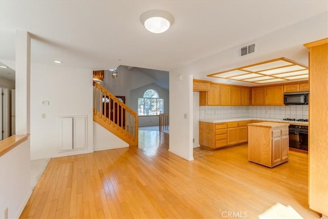 kitchen with light wood-type flooring, decorative backsplash, a center island, and black appliances