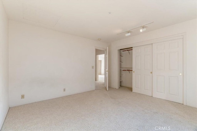 unfurnished bedroom with a closet, rail lighting, and light colored carpet