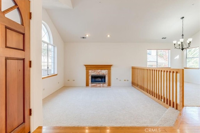 unfurnished living room featuring a high end fireplace, light colored carpet, lofted ceiling, and a notable chandelier