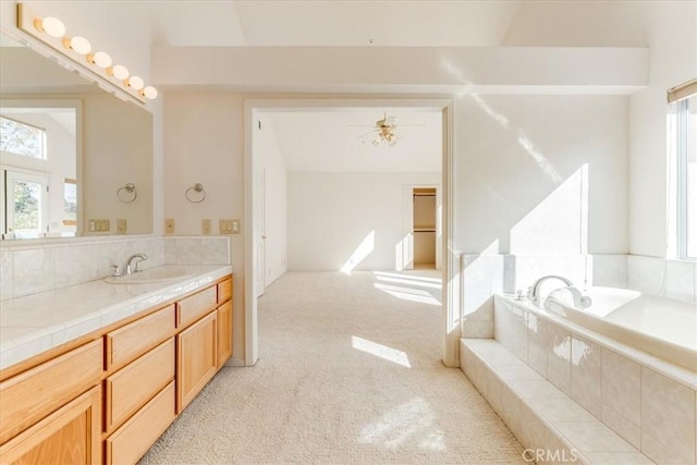 bathroom with a relaxing tiled tub, plenty of natural light, ceiling fan, and vanity