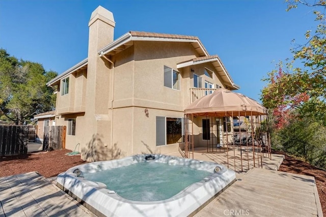 rear view of property featuring a balcony and an outdoor hot tub