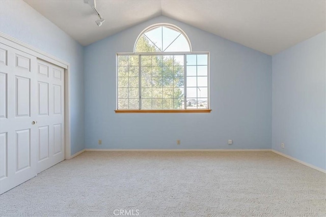 unfurnished bedroom featuring light carpet, a closet, rail lighting, and lofted ceiling