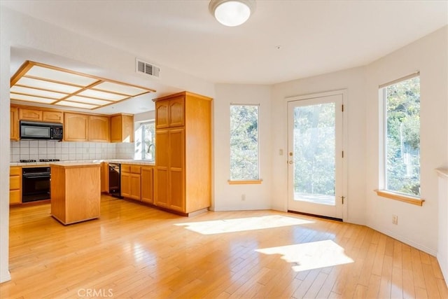 kitchen with light hardwood / wood-style flooring, a kitchen island, plenty of natural light, and black appliances