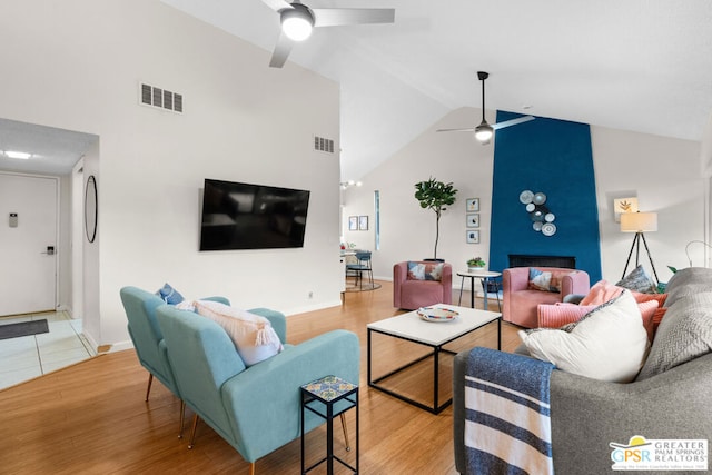 living room featuring ceiling fan, a large fireplace, wood-type flooring, and high vaulted ceiling