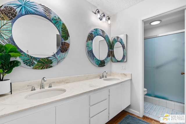 bathroom with vanity, a textured ceiling, hardwood / wood-style floors, toilet, and a shower with shower door