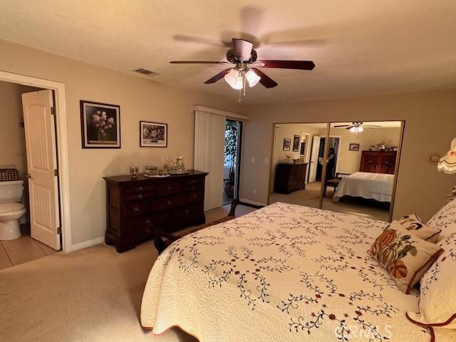 bedroom with connected bathroom, light colored carpet, access to exterior, and ceiling fan