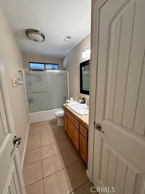 full bathroom with bath / shower combo with glass door, vanity, a textured ceiling, tile patterned floors, and toilet