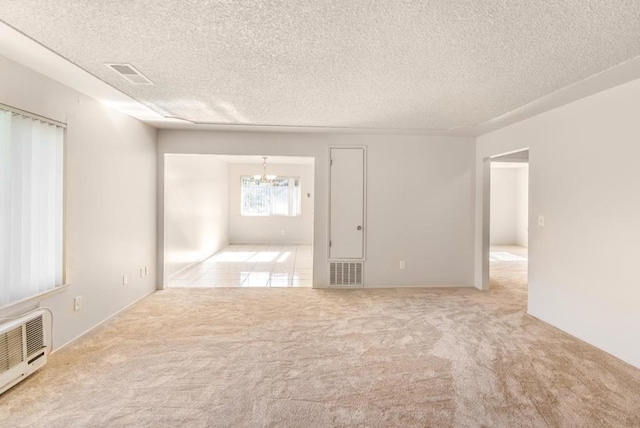 empty room with light colored carpet, a textured ceiling, and an inviting chandelier