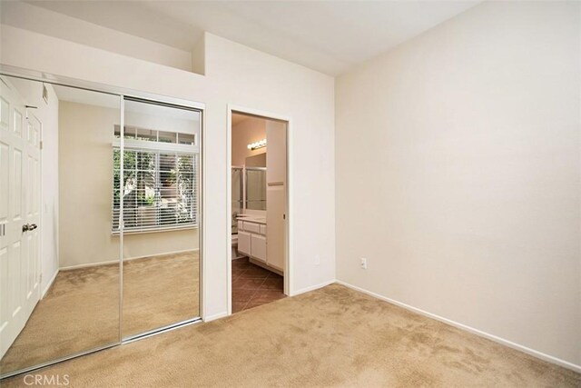 unfurnished bedroom featuring ensuite bath, light carpet, and a closet