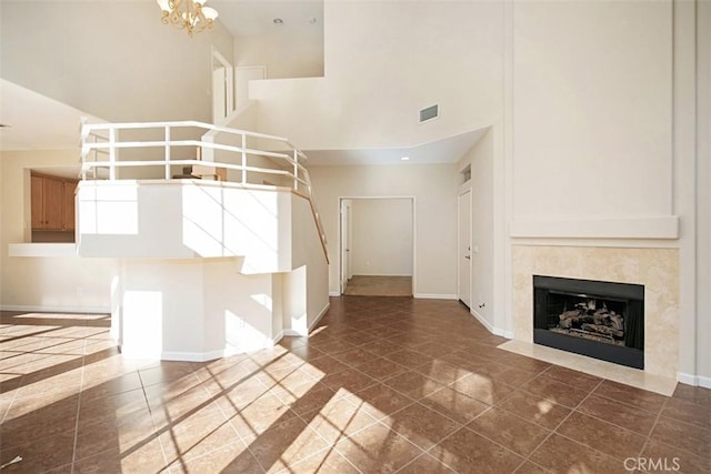 unfurnished living room featuring a chandelier, a high ceiling, and a tiled fireplace