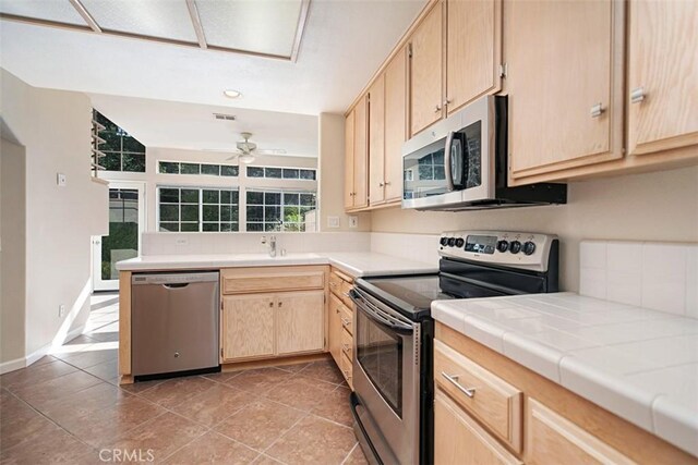 kitchen with appliances with stainless steel finishes, light brown cabinetry, tile patterned floors, ceiling fan, and tile counters