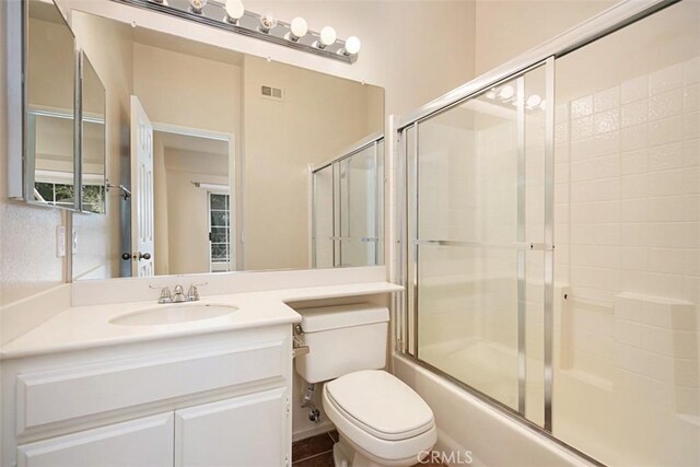 full bathroom featuring vanity, combined bath / shower with glass door, and toilet