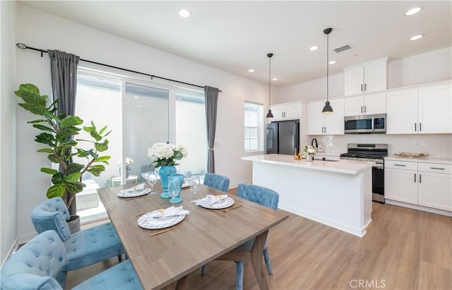 kitchen featuring white cabinetry, pendant lighting, decorative backsplash, a center island with sink, and appliances with stainless steel finishes