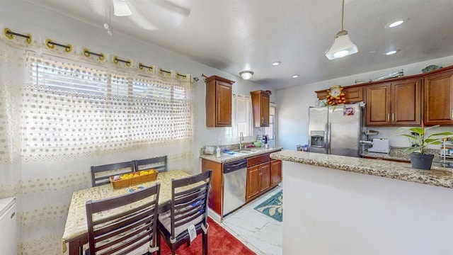 kitchen with appliances with stainless steel finishes, sink, light stone counters, and decorative light fixtures