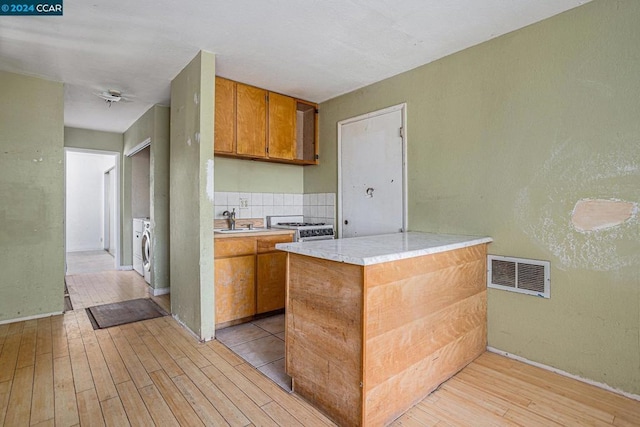 kitchen with sink, white range with gas stovetop, light hardwood / wood-style floors, decorative backsplash, and washer and dryer