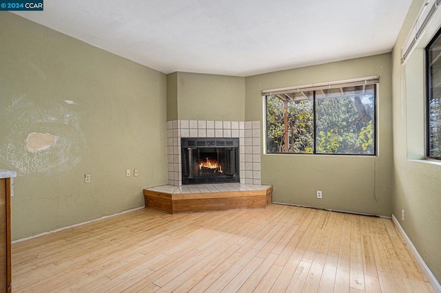 unfurnished living room with a tile fireplace and light hardwood / wood-style flooring