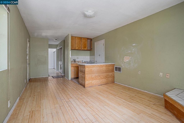 kitchen with sink, kitchen peninsula, light hardwood / wood-style floors, washer / dryer, and decorative backsplash