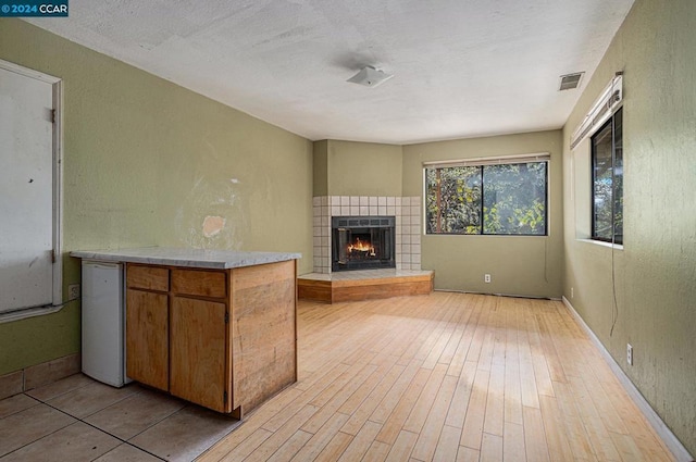 unfurnished living room with a tile fireplace, a textured ceiling, and light wood-type flooring