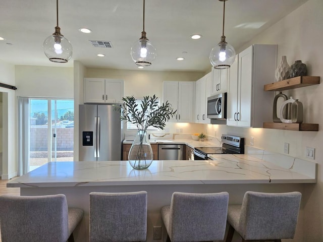 kitchen featuring kitchen peninsula, white cabinetry, light stone counters, and appliances with stainless steel finishes