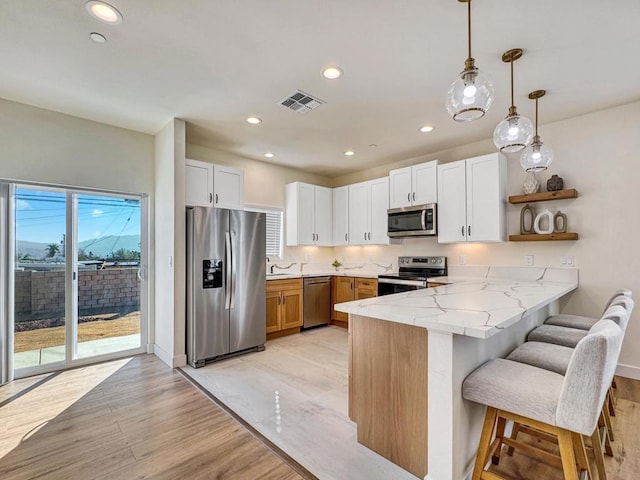 kitchen featuring kitchen peninsula, light stone countertops, stainless steel appliances, pendant lighting, and white cabinetry