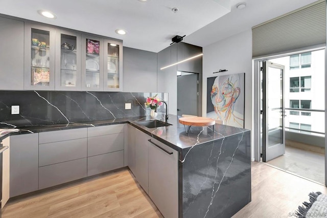 kitchen featuring gray cabinetry, sink, light hardwood / wood-style flooring, kitchen peninsula, and decorative backsplash