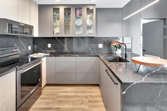 kitchen with sink, tasteful backsplash, gray cabinets, appliances with stainless steel finishes, and light wood-type flooring