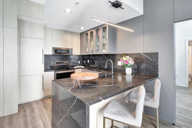 kitchen featuring sink, light hardwood / wood-style flooring, decorative backsplash, kitchen peninsula, and stainless steel appliances