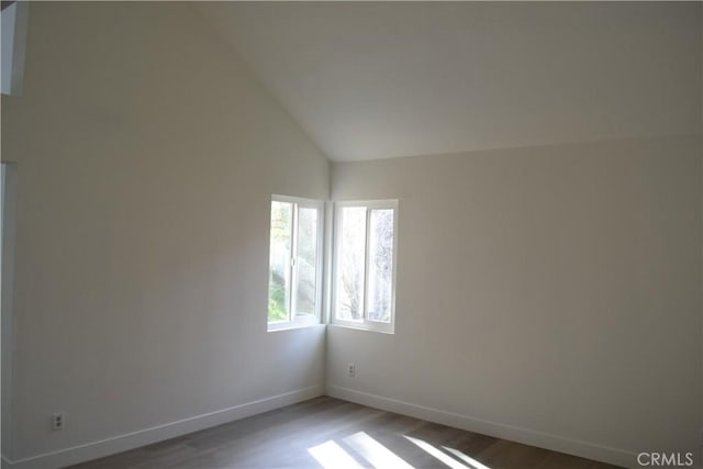 empty room featuring lofted ceiling, wood finished floors, and baseboards