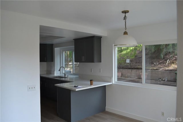 kitchen featuring pendant lighting, light countertops, a sink, dark cabinetry, and a peninsula