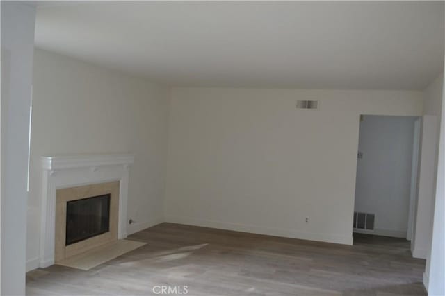 unfurnished living room featuring wood finished floors, a high end fireplace, visible vents, and baseboards